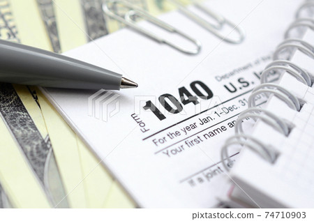 The pen, notebook and dollar bills is lies on the tax form 1040 U.S. Individual Income Tax Return. The time to pay taxes 74710903