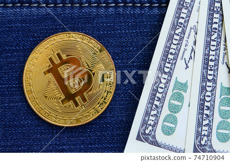 Golden Bitcoin and dollar bills lies on a blue jeans fabric. New virtual money. New crypto currency in the form of the coins 74710904