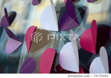 A lot of pink, purple and white paper hearts decorate the window of the house A lot of pink, purple and white paper hearts decorate the window of the house 74710905