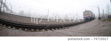 The Ukrainian suburban train rushes along the railway in a misty morning. Fisheye photo with increased distortion The Ukrainian suburban train rushes along the railway in a misty morning. Fisheye photo with increased distortion 74710927