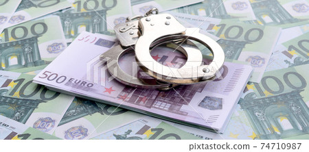 Police handcuffs lies on a set of green monetary denominations of 100 euros. A lot of money forms an infinite heap Police handcuffs lies on a set of green monetary denominations of 100 euros. A lot of money forms an infinite heap 74710987