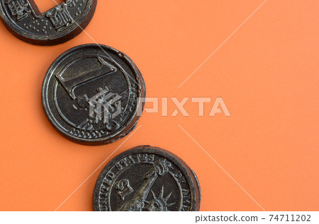 Three chocolate products in the form of Euro, USA and Japan coins lie on an orange plastic background. A model of cash coins in an edible form Three chocolate products in the form of Euro, USA and Japan coins lie on an orange plastic background. A model of cash coins in an edible form 74711202
