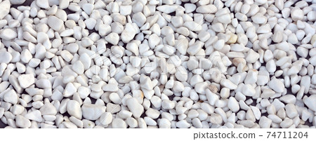 A lot of round and oval stones of white color lie on the ground in the garden A lot of round and oval stones of white color lie on the ground in the garden 74711204