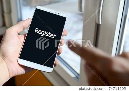 A person sees a white inscription on a black smartphone display that holds in his hand. Register A person sees a white inscription on a black smartphone display that holds in his hand. Register 74711205