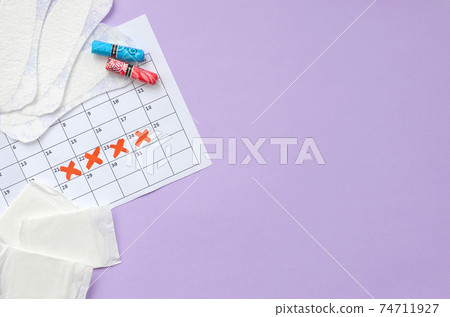 Menstrual pads and tampons on menstruation period calendar flat lay on lilac background 74711927