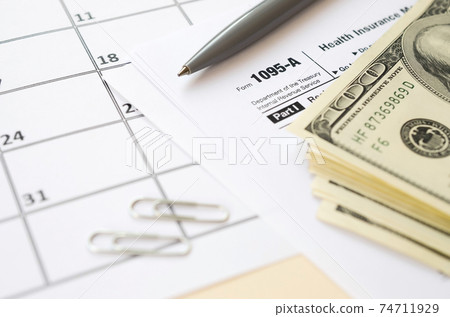 IRS Form 1095-A Health Insurance Marketplace Statement tax blank lies with pen and many hundred dollar bills on calendar page IRS Form 1095-A Health Insurance Marketplace Statement tax blank lies with pen and many hundred dollar bills on calendar page 74711929