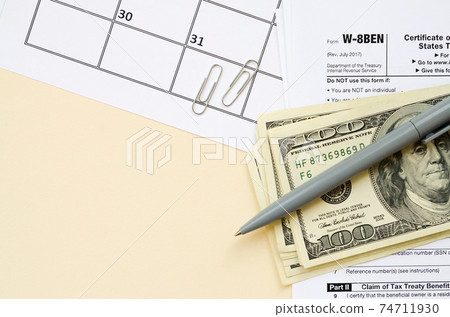IRS Form W-8BEN Certificate of foreign status of beneficial owner for United States tax withholding and reporting for individuals blank lies with pen and hundred dollar bills on calendar page 74711930