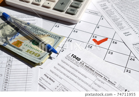 1040 Individual Income Tax Return blank with dollar bills, calculator and pen on calendar page with marked 15th April 74711955