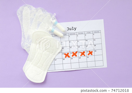 Menstrual pads and tampons on menstruation period calendar flat lay on lilac background Menstrual pads and tampons on menstruation period calendar flat lay on lilac background 74712018