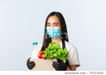 Covid-19, grocery store, employment, small business and preventing virus concept. Smiling cute asian female shop worker, cashier in medical mask and gloves taking care of your groceries order 74712033