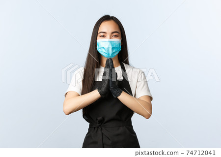 Covid-19, social distancing, small coffee shop business and preventing virus concept. Cute smiling asian employee, cafe barista in medical mask and gloves, hold hands in pleading gesture, pray 74712041