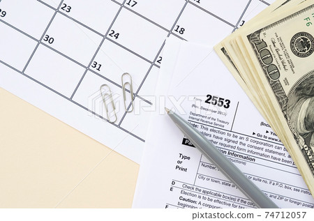 IRS Form 2553 Election by a Small Business Corporation tax blank lies with pen and many hundred dollar bills on calendar page 74712057