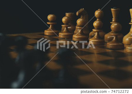 Black chess pieces against white chess pieces on a chessboard Black chess pieces against white chess pieces on a chessboard 74712272