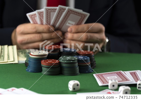Businessman at green playing table with gambling chips and cards playing poker and blackjack in casino 74712335