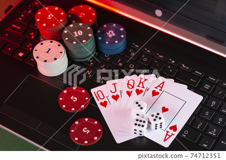 Online gaming platform, casino and gambling business. Cards, dice and multi-colored game pieces on laptop keyboard on green background Online gaming platform, casino and gambling business. Cards, dice and multi-colored game pieces on laptop keyboard on green background 74712351