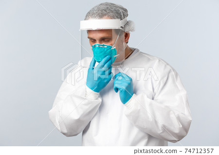 Covid-19, preventing virus, healthcare workers and vaccination concept. Tired doctor working in clinic with contaigned patients, sick coronavirus, fixing medical respirator while wearing PPE Covid-19, preventing virus, healthcare workers and vaccination concept. Tired doctor working in clinic with contaigned patients, sick coronavirus, fixing medical respirator while wearing PPE 74712357