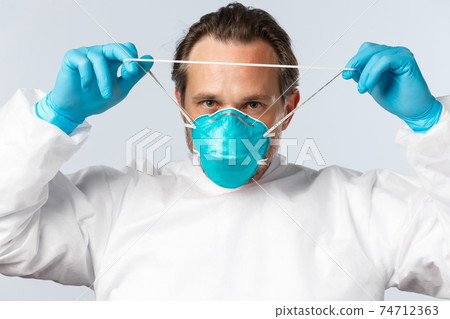 Covid-19, preventing virus, healthcare workers and vaccination concept. Close-up of serious professional doctor in personal protective equipment, wearing respirator before entering patient ward 74712363