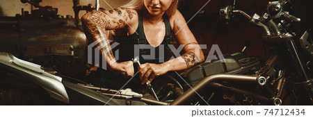 Blond woman mechanic repairing a motorcycle 74712434