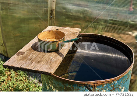 Rain barrel with water against the background of the greenhouse Rain barrel with water against the background of the greenhouse 74721552