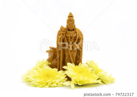 The wooden statue of Lord Murugan with yellow flowers is isolated on a white background The wooden statue of Lord Murugan with yellow flowers is isolated on a white background 74722317