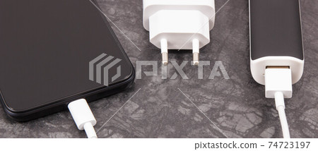 Black smartphone with connected plug of external powerbank. Mobile phone charging 74723197