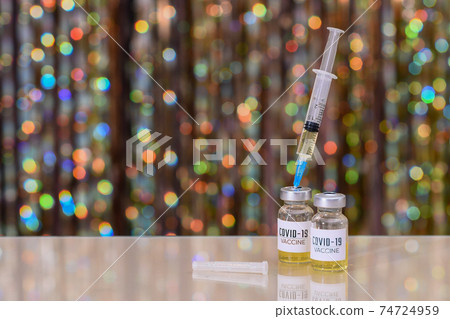 A bottle of of coronavirus vaccine. The syringe is inserted into a bottle with the covid-19 vaccine. On a shiny bokeh background.  74724959