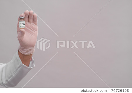 A bottle of covid-19 vaccine in the hands of a medical glove. Close-up. A bottle of covid-19 vaccine in the hands of a medical glove. Close-up. 74726198