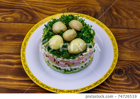 Traditional Russian layered salad "Mushroom Glade" from boiled potatoes, carrots, eggs, sausage, soft cheese, marinated mushrooms and mayonnaise on wooden table 74726519