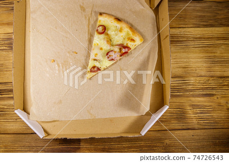 Last slice of pizza in cardboard box on a wooden table. Top view. Concept for home delivery of food, fast food, delivery of pizza 74726543