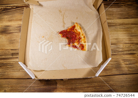 Bitten slice of pizza in cardboard box on a wooden table. Top view. Concept for home delivery of food, fast food, delivery of pizza 74726544