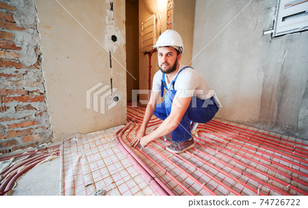 Bearded young man installing underfloor heating pipes. 74726722