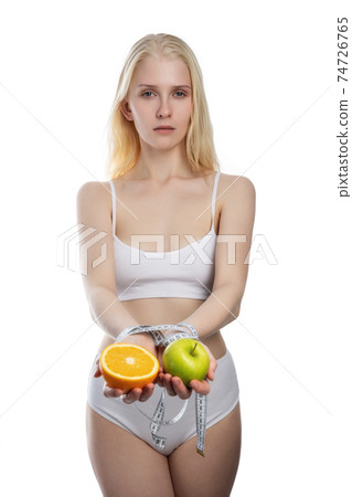 Apple and orange in female hands tied with turquoise measuring tape, isolated on white background 74726765