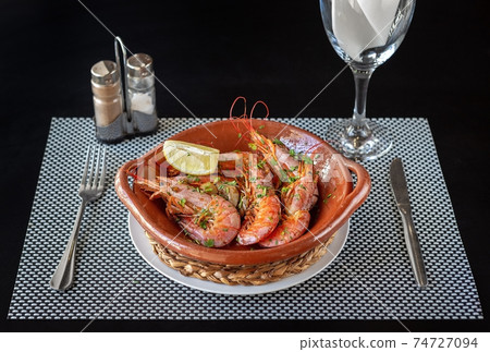 Cooked shrimp inside a clay bowl, cutlery on the sides and a glass of water. Composition of a meal ready to be eaten. 74727094