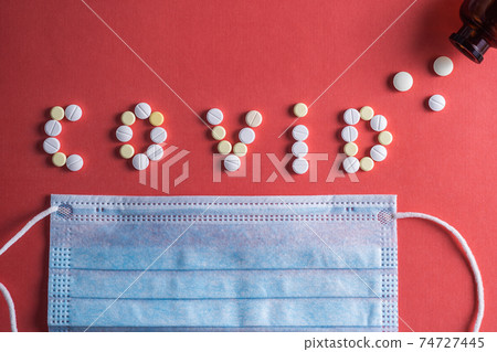 Inscription COVID-19 from white medical pills and surgical procedure medical face mask. Vaccine development concept. 74727445