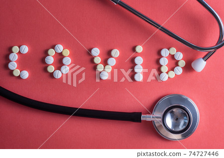 Flat lay of medicine pills shape as word covid 19 with syringe and pills on red background 74727446