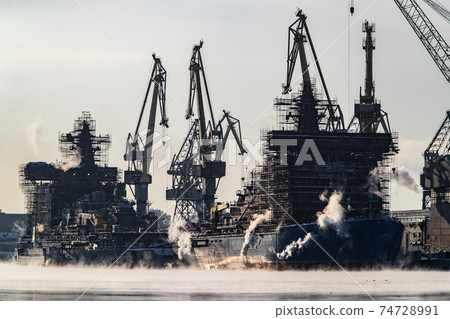Cranes of of the shipyard on a frosty winter day, steam over the Neva river, smooth surface of the river, mirror reflection on the water, ships under construction, trawlers, nuclear icebreakers 74728991