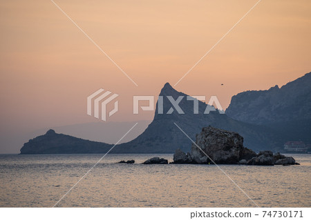 Sea coast with rocky cliffs. Seashore near a mountain with rocks and small waves. 74730171