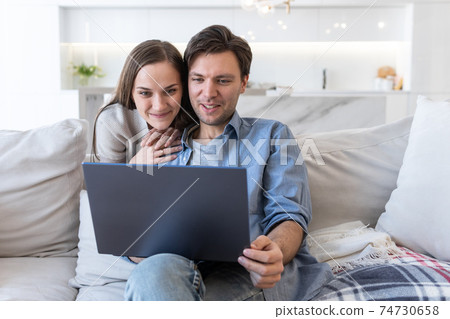 Cheerful couple looking at screen of laptop Cheerful couple looking at screen of laptop 74730658