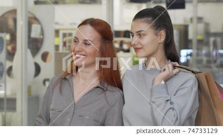 Two happy female friends smiling to the camera while shopping at the mall Two happy female friends smiling to the camera while shopping at the mall 74733129