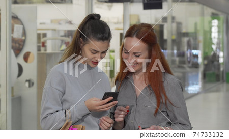 Two female friends using smart phone at the shopping mall 74733132