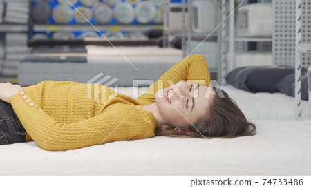 Happy young woman enjoying lying on new mattress at furniture store 74733486