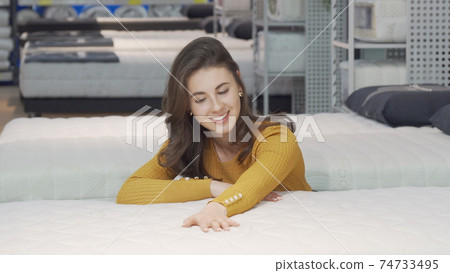 Beautiful happy woman examining orthopedic mattress on sale 74733495