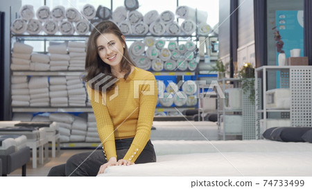 Beautiful woman smiling to the camera sitting on a new bed at furniture store Beautiful woman smiling to the camera sitting on a new bed at furniture store 74733499