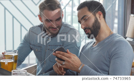 Two male friends using smart phone while drinking beer together 74733965