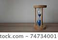 Pouring sand in an hourglass standing on an a wood desk. 74734001