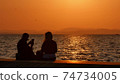 Silhouette of a young couple taking a selfie at sunset, with a sea and sunset in the background. 74734005