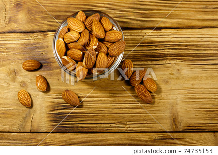 Almonds in glass bowl on a rustic wooden table. Top view 74735153