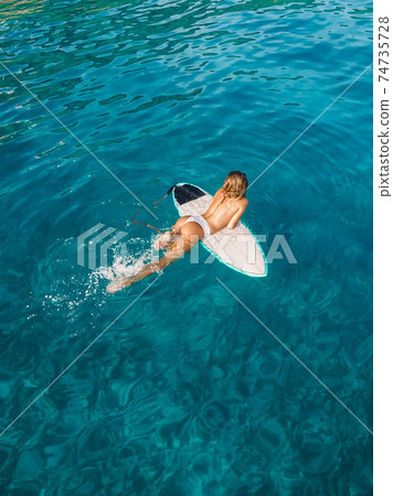 Attractive surfer woman relaxing on surfboard in blue ocean. Aerial view with surf girl 74735728