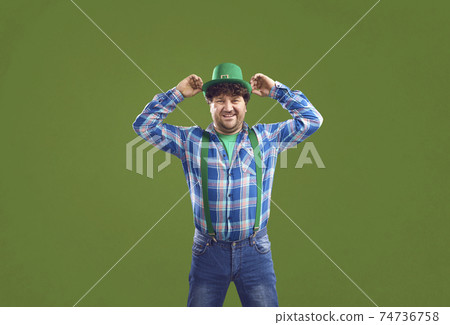 Happy man puts on a green hat and smiles standing isolated on a colour background Happy man puts on a green hat and smiles standing isolated on a colour background 74736758