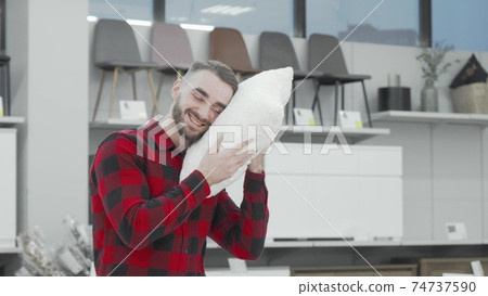 Handsome young man choosing new pillow to buy at furnishings store Handsome young man choosing new pillow to buy at furnishings store 74737590